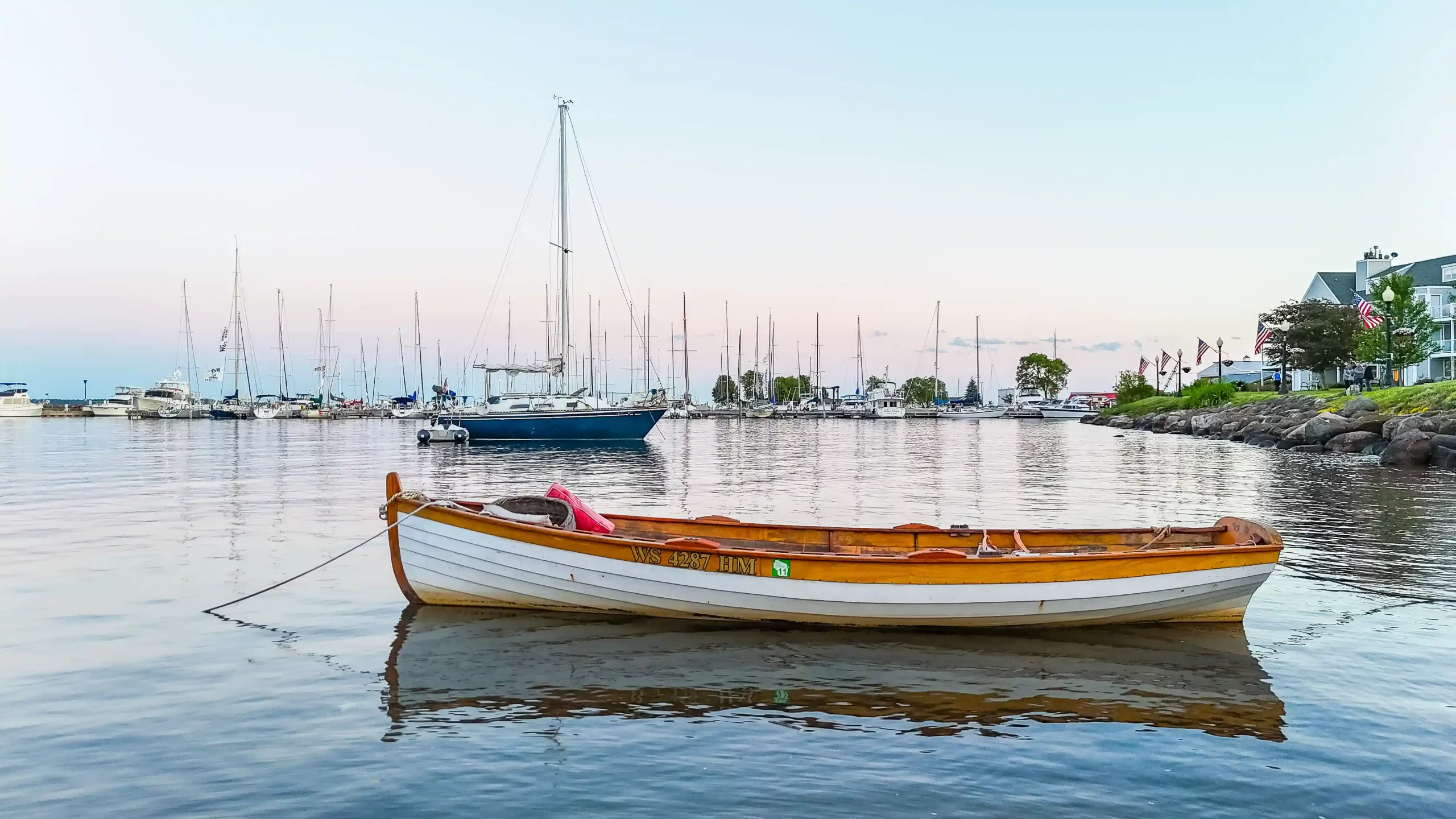 A white and wooden colored canoe sits in front of a marina of sail boats and yachts